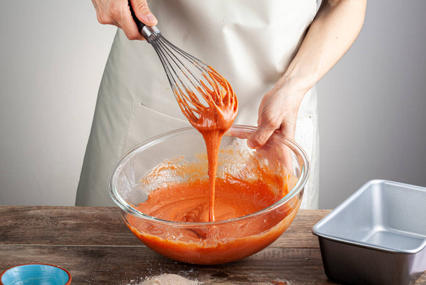 Женщина смешивает кроваво-оранжевый торт в стеклянную миску с помощью воздушного шарика. Концепция приготовления пищи, домашний рецепт, пищевая окраска, добавки.  - Фото, изображение