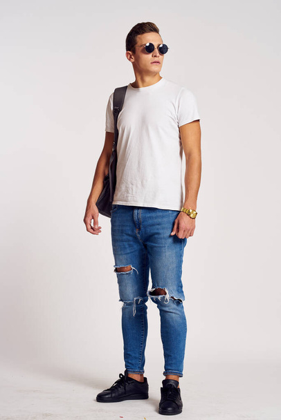 a man with a backpack on his back in jeans t-shirt full length sneakers and glasses on his face - Foto, afbeelding