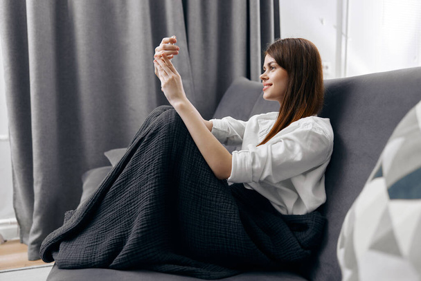 žena sedí na šedé pohovce s telefonem před očima boční pohled  - Fotografie, Obrázek