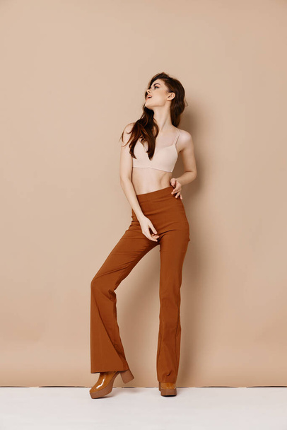fashionable woman in trousers in a t-shirt and high-heeled shoes on a beige background gesturing with her hands - Foto, Imagem