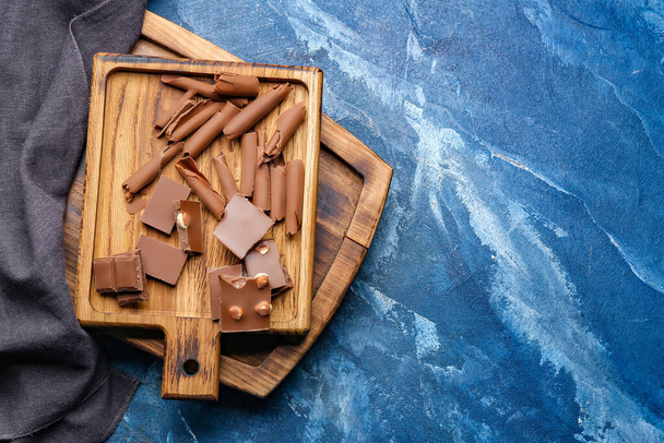 Wooden board with tasty chocolate curls on color background - Photo, Image