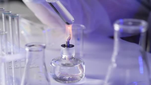 Close-up of the hand of a medical scientist in protective clothing and gloves holding a test tube with a solution over the burner fire. Experiments in the laboratory to find a cure for the virus. - Footage, Video