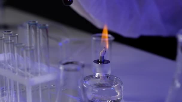 Close-up of hand of pharmaceutical scientist in protective clothing and gloves holding test tube with chemical material over burner fire. Experiments in  laboratory to find vaccine against the virus. - Footage, Video