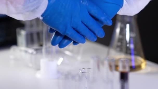 İki araştırmacı bilim adamı, laboratuvar ekipmanlarının arka planına karşı koruyucu eldivenlerle el sıkışıyor. Bilim insanları koronavirüs için ilaç bulmada başarı ile seviniyor - Video, Çekim