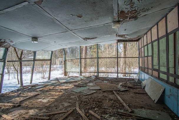 Verlaten oude eetkamer in een kamp in het bos met een dak dat instortte tijdens de winterdag. - Foto, afbeelding