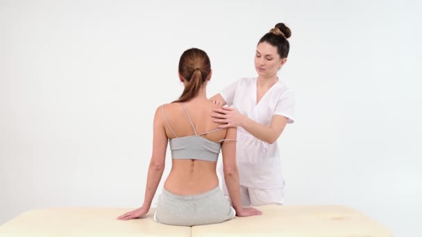 Fisioterapeuta Masajeando el hombro de una paciente. Vista sobre el hombro del masajista realizando masaje de tejido profundo. Imágenes de 4k. cerrar vídeo sobre fondo blanco - Imágenes, Vídeo