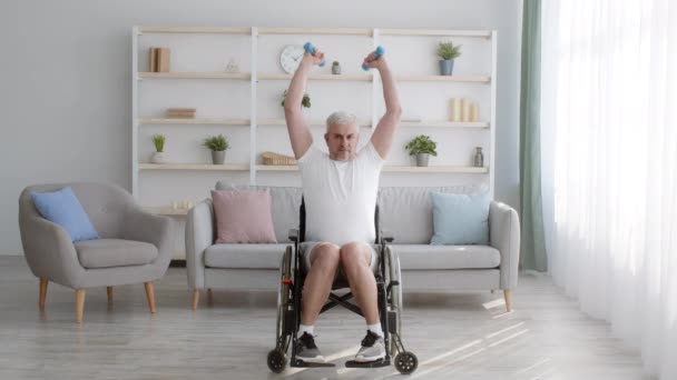 Heikentynyt mies harjoittelee käsipainoilla istuen pyörätuolissa kotona - Materiaali, video