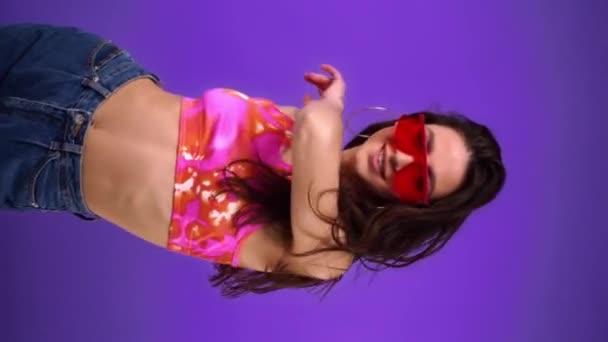 Mujer alegre y elegante en gafas de sol bailando aislado en púrpura  - Metraje, vídeo