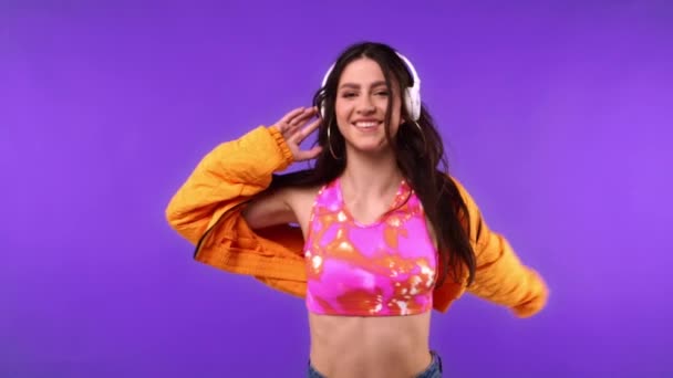 Αργή κίνηση χαρούμενης γυναίκας με ακουστικά που χορεύει απομονωμένη σε μωβ  - Πλάνα, βίντεο