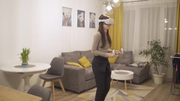 VRヘッドセットを持つ幸せな若い女性がゲームをプレイし、 VRコントローラーを使用して戦っています - 映像、動画