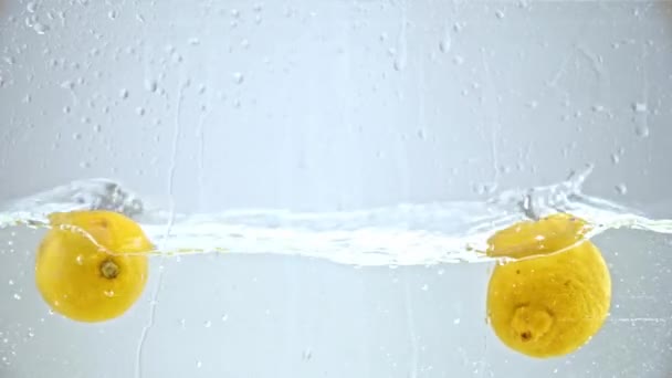 zpomalený pohyb celých citronů tekoucích ve vodě na modré - Záběry, video
