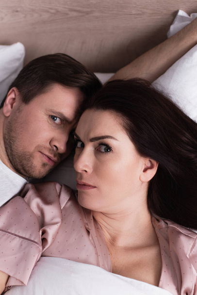 High angle view of adult couple looking at camera on bed  - Foto, immagini