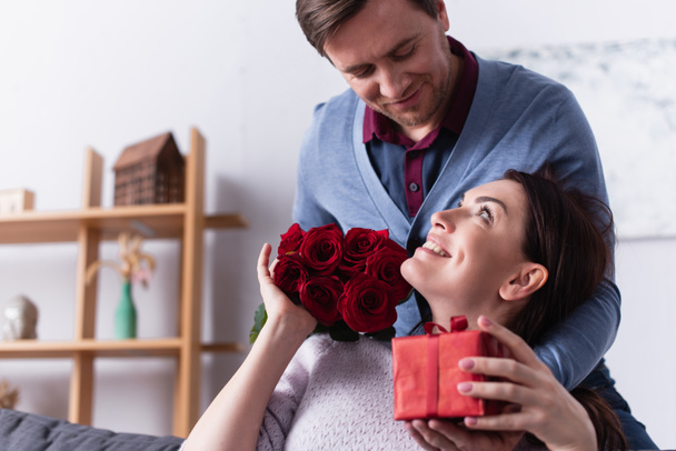 Woman with present and flowers looking at husband  - Photo, Image