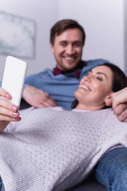 Woman using cellphone near husband on blurred background  - Фото, зображення