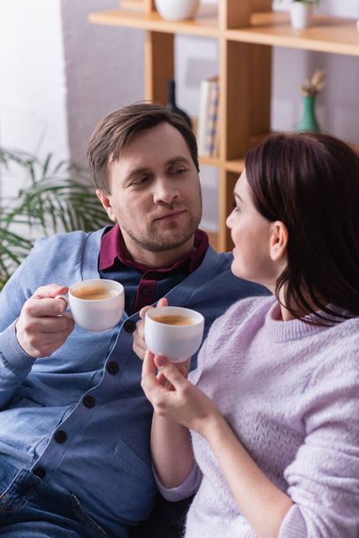Mężczyzna z filiżanką kawy patrząc na żonę na niewyraźnym pierwszym planie  - Zdjęcie, obraz