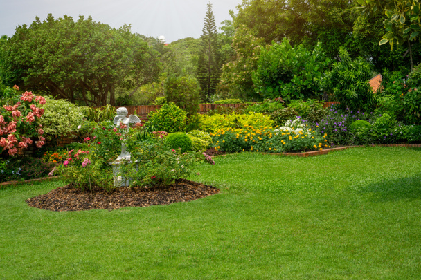Zurück und Vorgarten Englischer Landhausgarten, glatter grüner Rasenrasen, bunte Blütenpflanze und orangefarbene Ziegelmauer, immergrüne Bäume im Hintergrund, in guter Pflege im Park gepflegt  - Foto, Bild