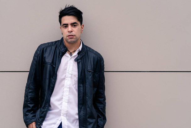 Half-length photograph of a young Latino guy leaning against a plain colored wall. Urban clothing. - Photo, Image