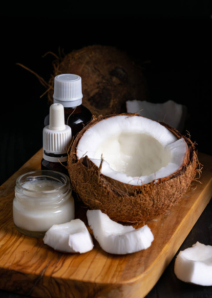 coconut and oil bottles on a wooden board on a black background - Photo, Image