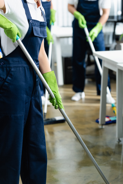 Cropped view of cleaner in rubber gloves holding mop in office on blurred background  - Foto, Bild