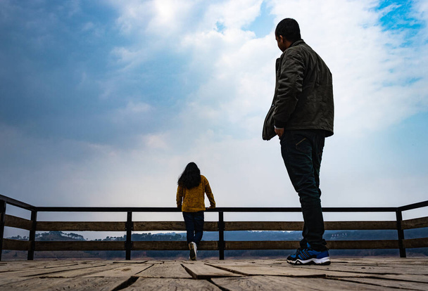 jonge jongen op zoek naar zijn vriendin op houten brug met bewolkte hemel vanuit lage hoek leidende lijn en ruimte voor tekst - Foto, afbeelding