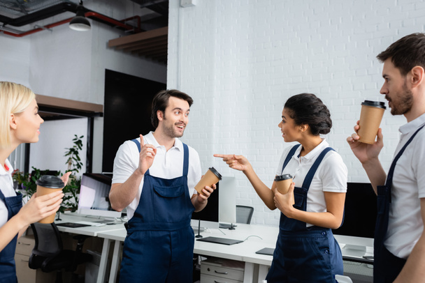 African american cleaner with coffee to go pointing at colleague in office  - Photo, Image