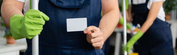Cropped view of cleaner with mop holding empty card in office, banner  - Fotografie, Obrázek