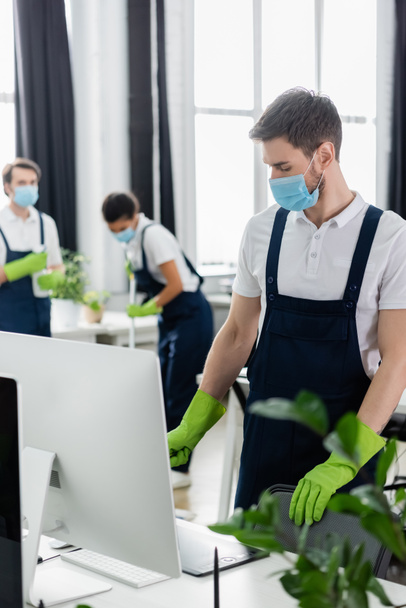 Cleaner in medical mask standing near computer and graphic tablet in office  - Photo, Image