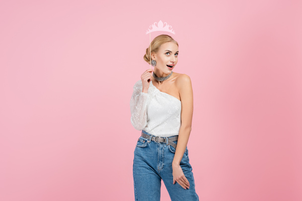 amazed and stylish woman holding paper crown on stick isolated on pink - Photo, Image