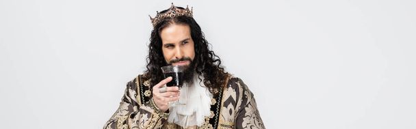 hispanic king in medieval clothing and crown holding glass of red wine isolated on white, banner - Photo, Image