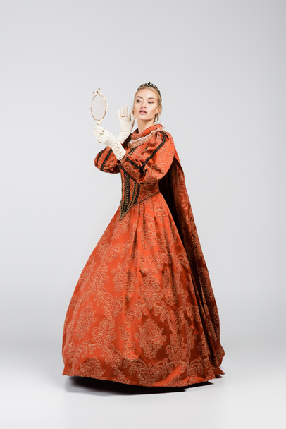 longitud completa de la reina rubia en vestido y corona mirando el espejo en blanco  - Foto, Imagen