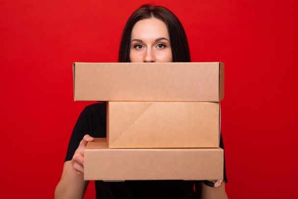 Kırmızı arka planda karton kutuları olan genç bir kadın. - Fotoğraf, Görsel