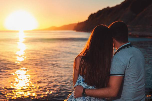 Egy fiatal szerelmespár, egy férfi és egy nő, ülnek a parton és nézik a naplementét. Visszapillantás. A Valentin-nap fogalma. - Fotó, kép