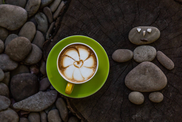 Cappuccino in a green cup with a beautiful pattern, on a wooden and stone background. Coffee art. - Photo, Image