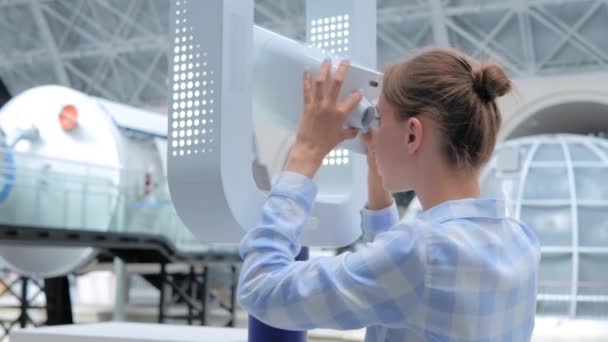 Nuori nainen katselee valkoisen kaukoputken läpi ja tutkii näyttelyä - Materiaali, video
