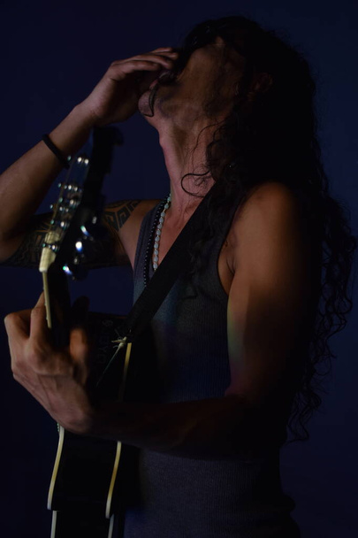 Schöner Mann mit langen lockigen Haaren spielt Gitarre fröhliches Lachen voller Glück, schwarzer Hintergrund Studiofoto - Foto, Bild