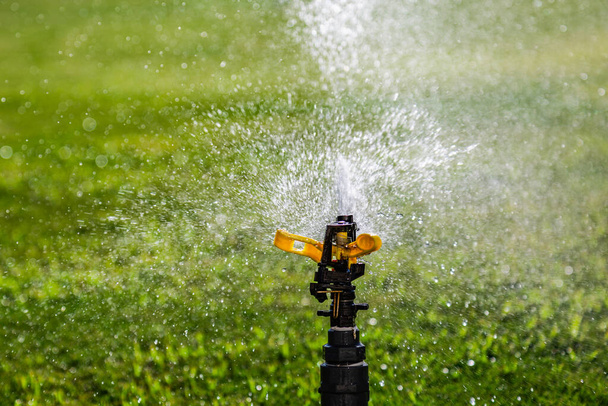 Автоматический разбрызгиватель воды на фоне зеленой травы. Поворотная голова - Фото, изображение