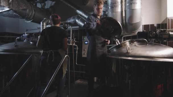 Fotografía en cámara lenta de un par de trabajadores cerveceros que controlan la producción de cerveza. Hombre con colega hembra abriendo caldera comprobando proceso de fermentación - Imágenes, Vídeo