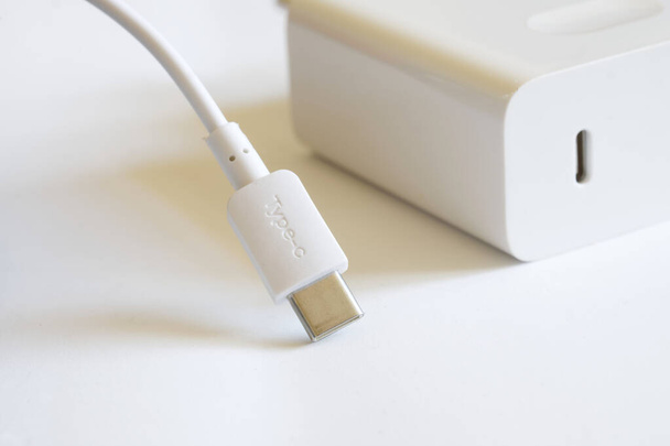 Белый разъем USB типа C с проводом лежит на светлом фоне рядом с белым блоком питания и быстрым зарядным устройством. Концепция современных технологий и чистой энергии. Макро. Селективное фокусирование - Фото, изображение