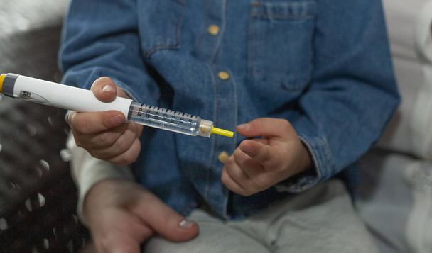 Het kleine meisje injecteert zichzelf met insuline. Het meisje geeft een injectie. Werelddiabetesdag. - Foto, afbeelding