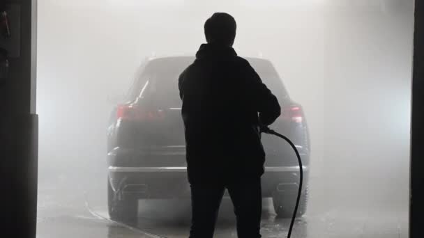 Autonpesu ja yksityiskohtaisesti. Ammattimainen työntekijä pesee mustaa autoa painepesurilla autopesulassa. - Materiaali, video
