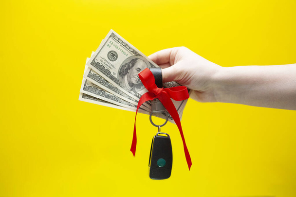 Γυναικείο χέρι που κρατά τα χρήματα και τα κλειδιά του αυτοκινήτου στο κίτρινο φόντο - Φωτογραφία, εικόνα
