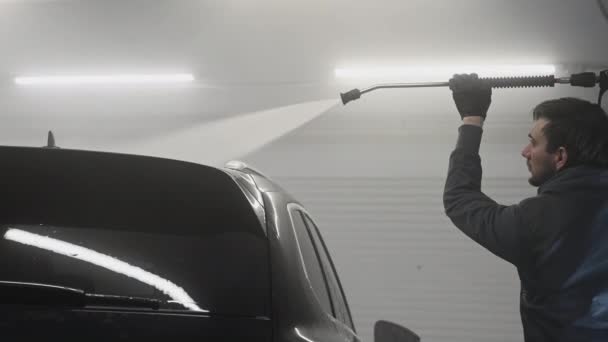 Autonpesu ja yksityiskohtaisesti. Ammattimainen työntekijä pesee mustaa autoa painepesurilla autopesulassa. - Materiaali, video