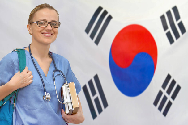 韓国の旗の背景に手に聴診器と本を持つ女性学生の医師。医学教育の概念。韓国で医学を学ぶ - 写真・画像