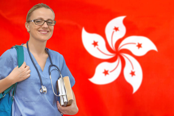 香港の旗の背景に手に聴診器と本を持つ女性学生の医師。医学教育の概念。香港で医学を学ぶ - 写真・画像