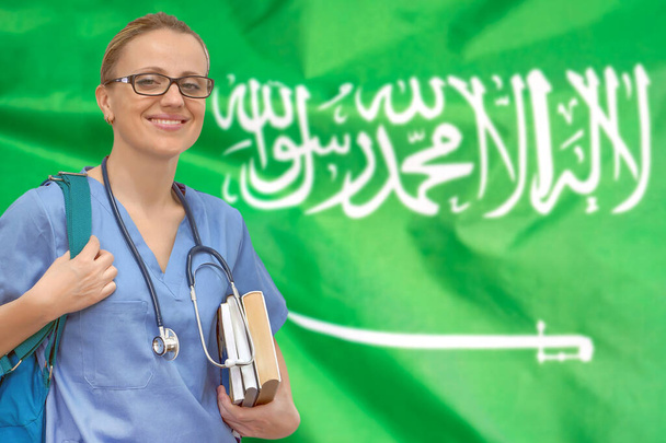Doctora estudiante con estetoscopio y libros en la mano sobre el fondo de la bandera de Arabia Saudita. Concepto de educación médica. Formación médica en Arabia Saudita - Foto, imagen