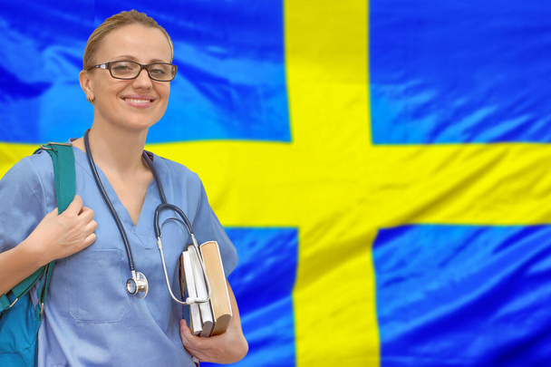 Étudiante médecin avec stéthoscope et livres en main sur le fond du drapeau suédois. Concept d'éducation médicale. L'apprentissage médical en Suède - Photo, image
