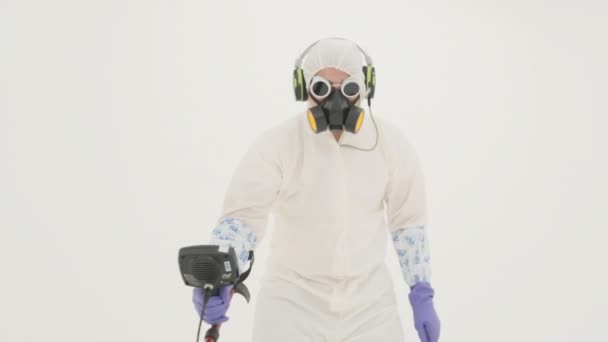 Fehér vegyi védőruhás férfi, gázálarc és lila gumikesztyű, fémdetektorral. Fehér háttérrel filmezve. - Felvétel, videó