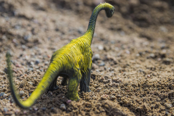 おもちゃの恐竜が小石で地面に沿って歩いています。おもちゃの外交官が通りに。子供は恐竜を連れて通りに出た。 - 写真・画像