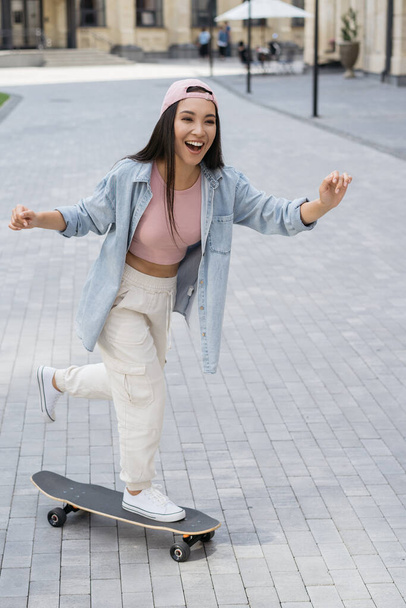 Joven mujer asiática emocional montando en monopatín al aire libre. Concepto de estilo activo - Foto, Imagen