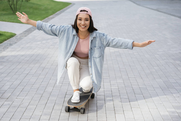 Schöne asiatische Frau in lässiger Kleidung, die auf dem Skateboard unterwegs ist und Spaß im Freien hat. Extremes Hobby, aktives Lebensstil-Konzept  - Foto, Bild